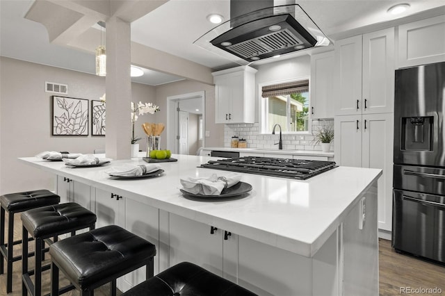 1120 S Harrison St, Denver, CO 80210 - kitchen with appliances with stainless steel finishes, island range hood, white cabinets, a breakfast bar area, and backsplash