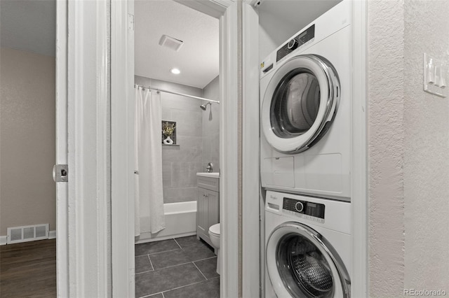 1120 S Harrison St, Denver, CO 80210 - washroom featuring stacked washing machine and dryer, a textured wall, and dark tile patterned floors