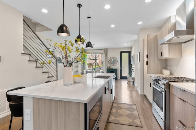 3885 Vrain St, Denver, CO 80212 - kitchen with appliances with stainless steel finishes, wall chimney exhaust hood, light brown cabinetry, an island with sink, and light wood-type flooring