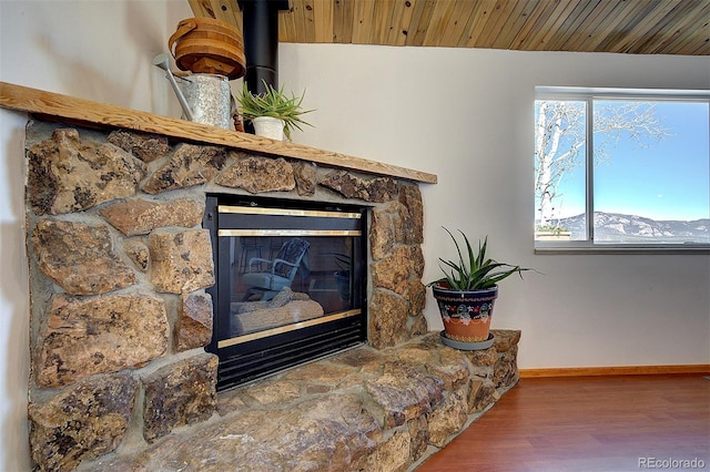 room details with wood ceiling, baseboards, wood finished floors, and a stone fireplace