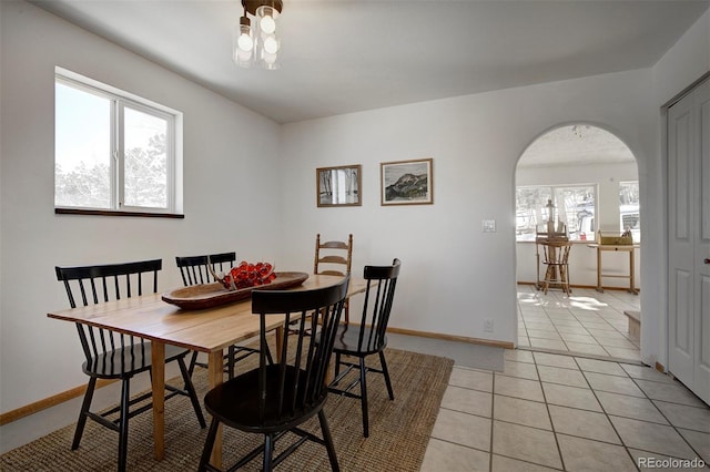 dining room with arched walkways, light tile patterned floors, and baseboards