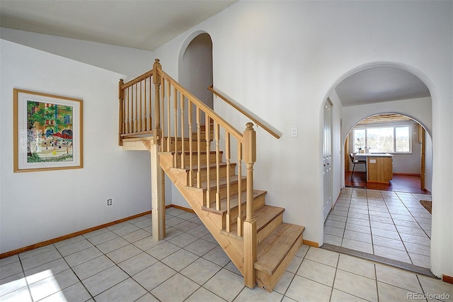 stairs with arched walkways, tile patterned flooring, and baseboards