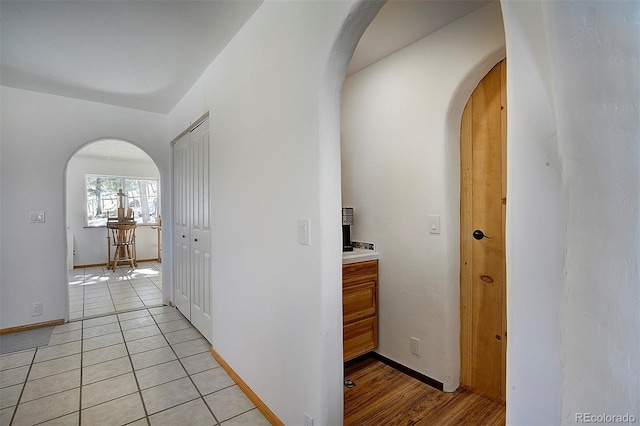 hall featuring arched walkways, light tile patterned floors, and baseboards