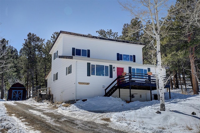 view of front facade featuring an outdoor structure, stairway, a wooden deck, and a storage unit