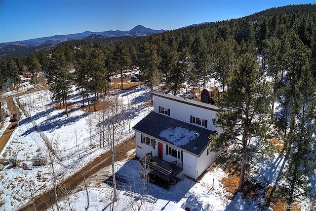 snowy aerial view featuring a mountain view and a view of trees