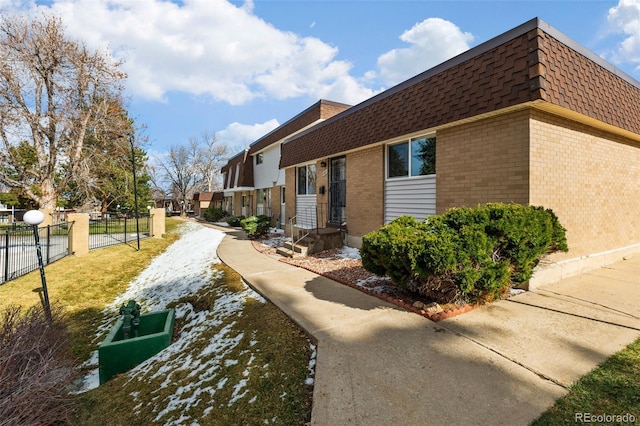 view of property exterior featuring mansard roof, fence, brick siding, and roof with shingles