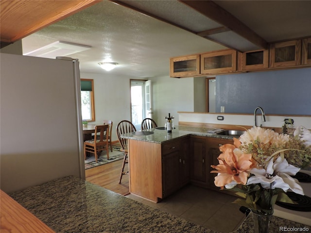 kitchen featuring refrigerator, sink, light tile patterned floors, a textured ceiling, and kitchen peninsula