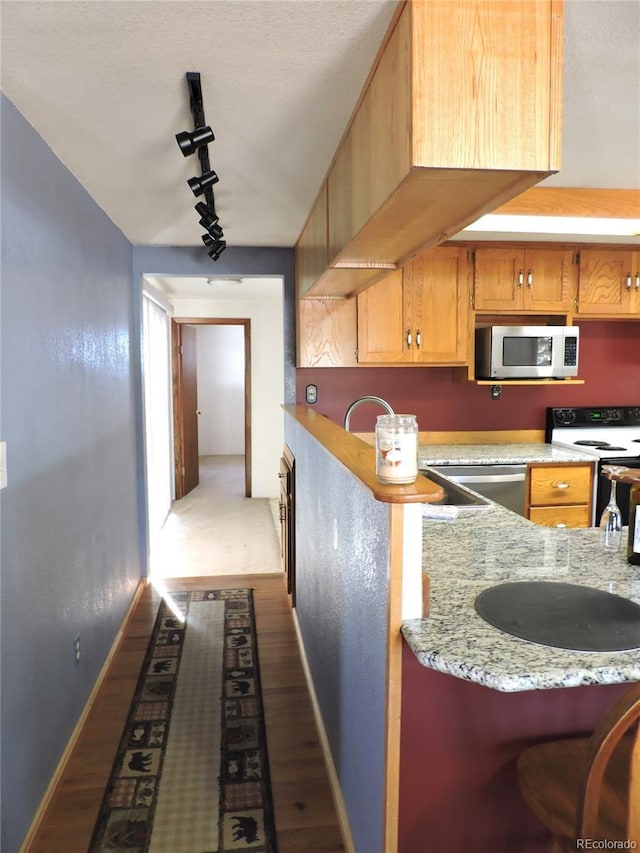 kitchen featuring rail lighting, light stone counters, white electric range oven, dark hardwood / wood-style flooring, and kitchen peninsula