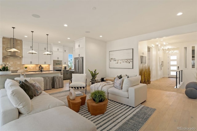 living room with an inviting chandelier, sink, and light hardwood / wood-style flooring