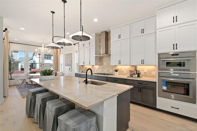 kitchen featuring white cabinetry, decorative light fixtures, a center island with sink, and wall chimney range hood