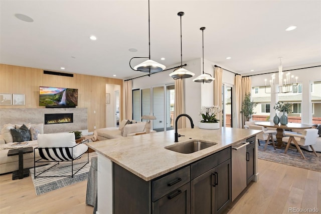 kitchen featuring pendant lighting, sink, light hardwood / wood-style flooring, light stone counters, and a center island with sink