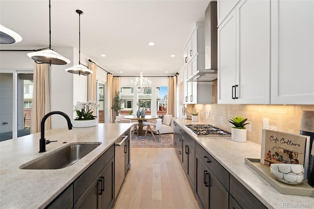 kitchen featuring sink, hanging light fixtures, wall chimney exhaust hood, white cabinets, and stainless steel gas stovetop