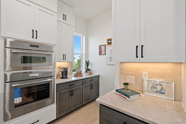 kitchen featuring backsplash, light wood-type flooring, double oven, and white cabinets