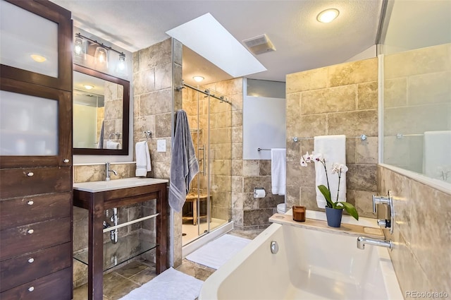 bathroom with vanity, vaulted ceiling with skylight, tile walls, a textured ceiling, and shower with separate bathtub