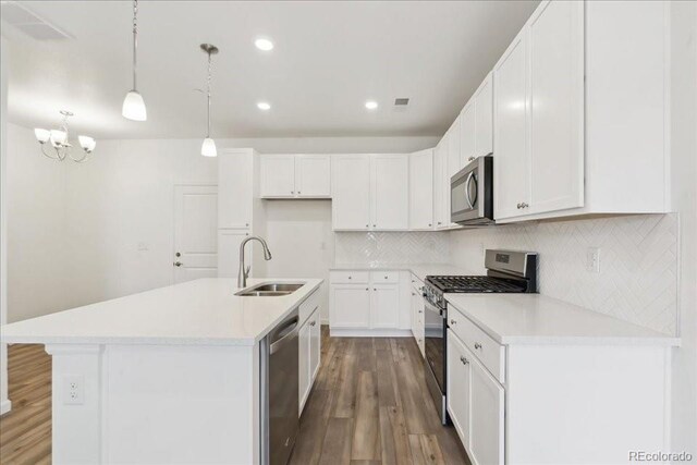 6902 Huddersfield Ln, Castle Pines, CO 80108 - kitchen featuring appliances with stainless steel finishes, a sink, wood finished floors, white cabinetry, and a kitchen island with sink