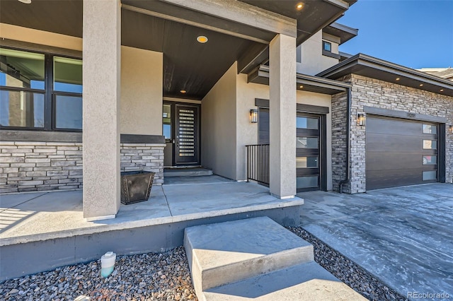 view of exterior entry featuring concrete driveway, an attached garage, stone siding, and stucco siding