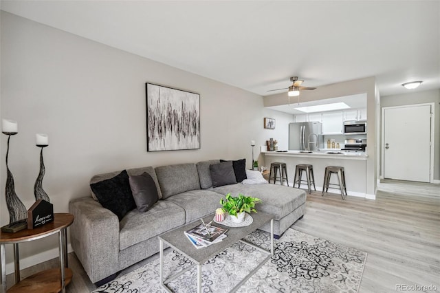 living area with light wood finished floors, ceiling fan, and baseboards