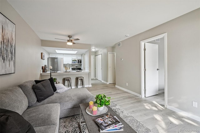 living area with ceiling fan, light wood-style flooring, visible vents, and baseboards