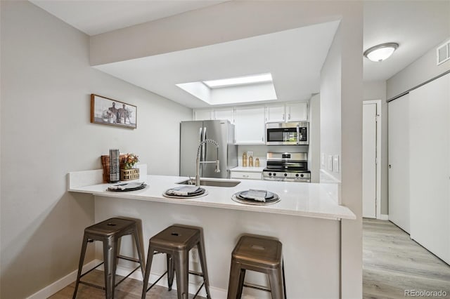 kitchen with a skylight, a breakfast bar, a peninsula, stainless steel appliances, and light countertops