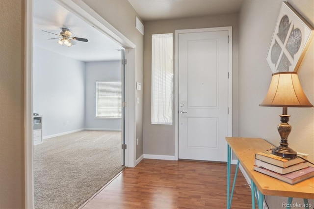 entryway featuring wood finished floors, baseboards, ceiling fan, and carpet floors