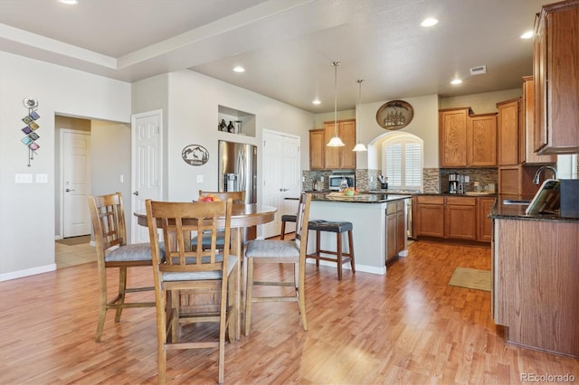 kitchen featuring appliances with stainless steel finishes, a sink, tasteful backsplash, light wood finished floors, and brown cabinets