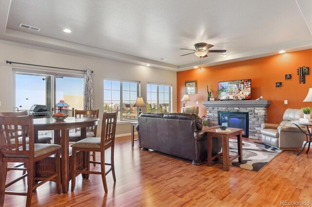 living room with a ceiling fan, light wood-style floors, a fireplace, a raised ceiling, and recessed lighting
