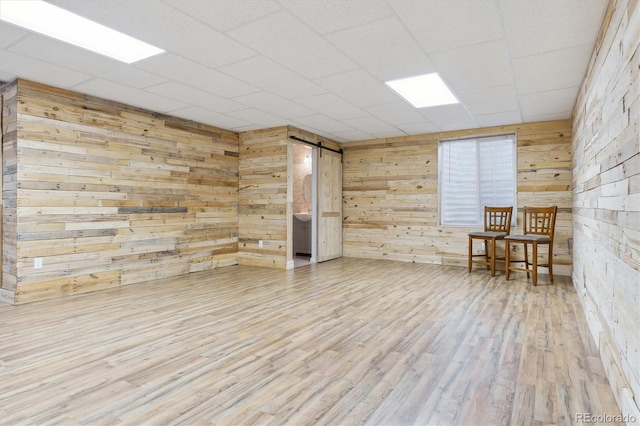 unfurnished room with a barn door, wood walls, and wood finished floors