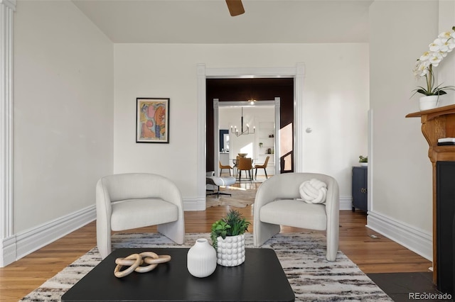 living area with ceiling fan with notable chandelier and wood-type flooring