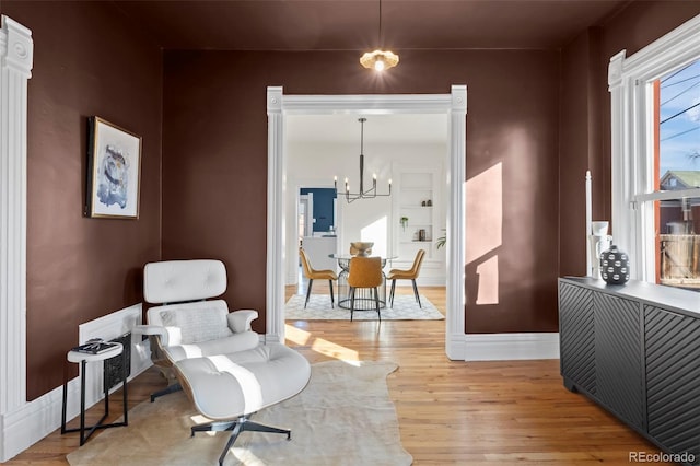 living area with an inviting chandelier, built in features, and light hardwood / wood-style floors