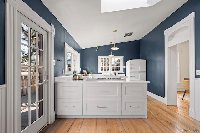 kitchen featuring white cabinetry, vaulted ceiling, hanging light fixtures, white fridge, and light hardwood / wood-style floors