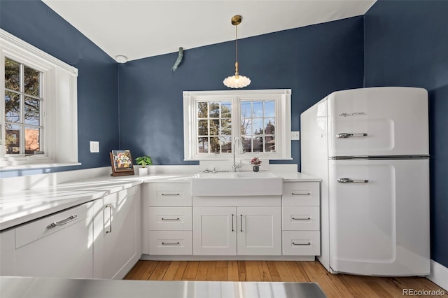 kitchen featuring sink, white cabinets, hanging light fixtures, white fridge, and light hardwood / wood-style floors