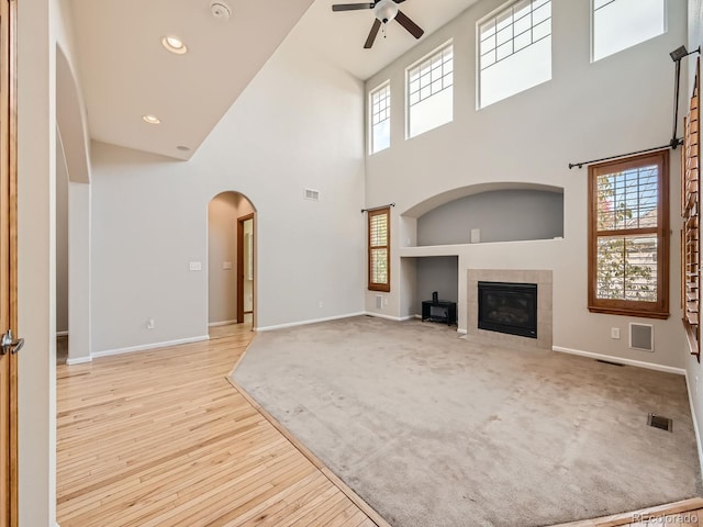 unfurnished living room with a high ceiling, light hardwood / wood-style flooring, a fireplace, and ceiling fan