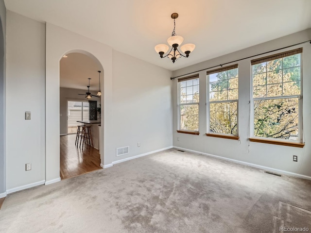 carpeted empty room with a healthy amount of sunlight and ceiling fan with notable chandelier