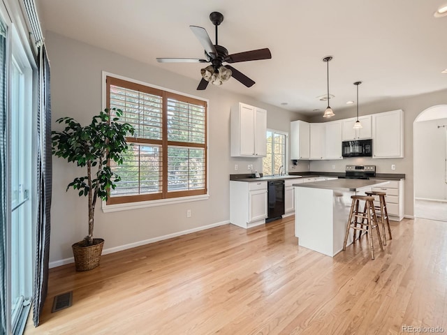 kitchen with black appliances, a center island, light hardwood / wood-style floors, white cabinets, and a breakfast bar