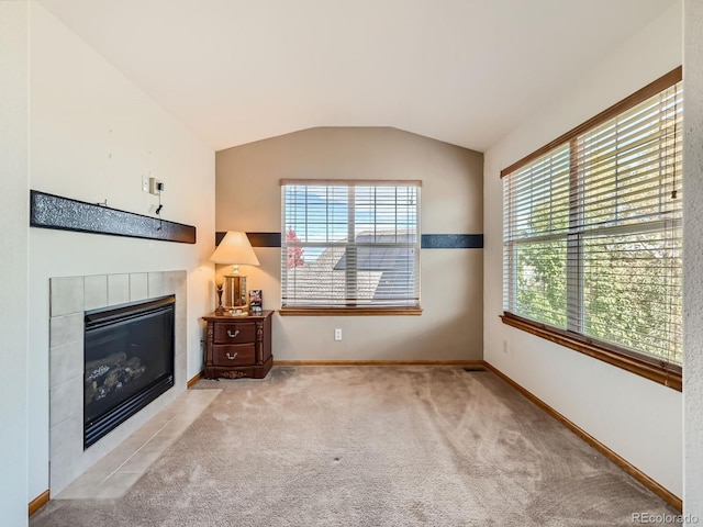 unfurnished living room featuring vaulted ceiling, a wealth of natural light, a tile fireplace, and light colored carpet