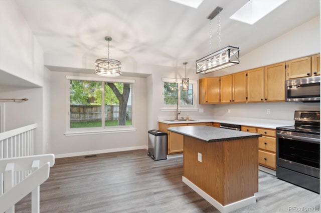 kitchen with sink, stainless steel appliances, a center island, decorative light fixtures, and light wood-type flooring