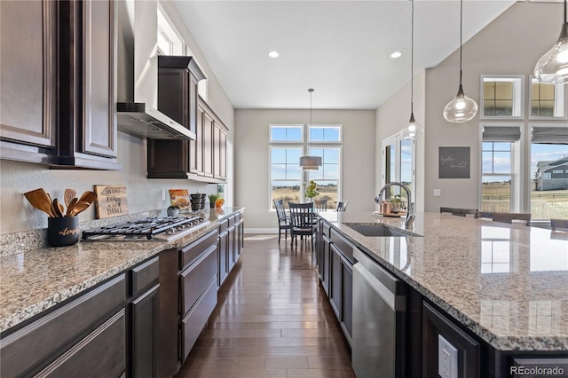 kitchen with stainless steel appliances, sink, dark hardwood / wood-style flooring, wall chimney range hood, and hanging light fixtures