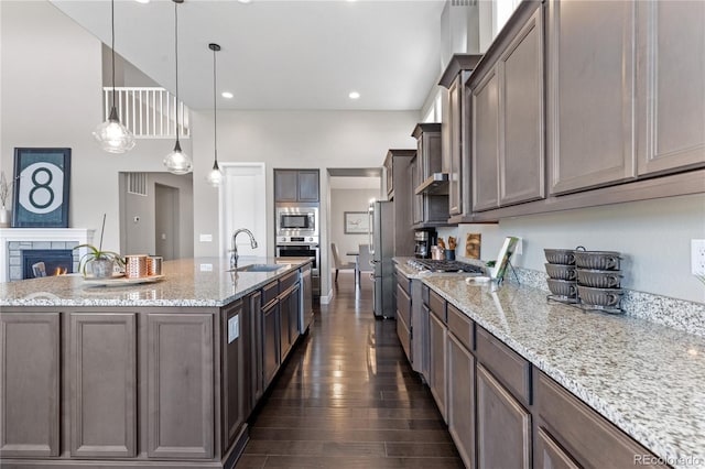 kitchen featuring decorative light fixtures, dark wood-type flooring, a center island with sink, light stone countertops, and sink