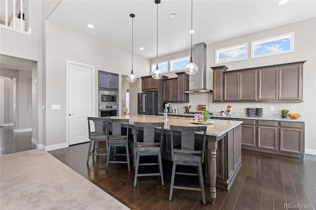 kitchen with stainless steel appliances, dark hardwood / wood-style flooring, a kitchen bar, wall chimney range hood, and decorative light fixtures