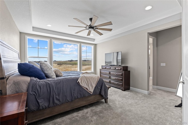 bedroom with light carpet, ceiling fan, a tray ceiling, and multiple windows