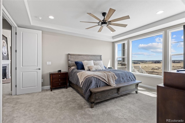 bedroom featuring light colored carpet, ceiling fan, a raised ceiling, and multiple windows