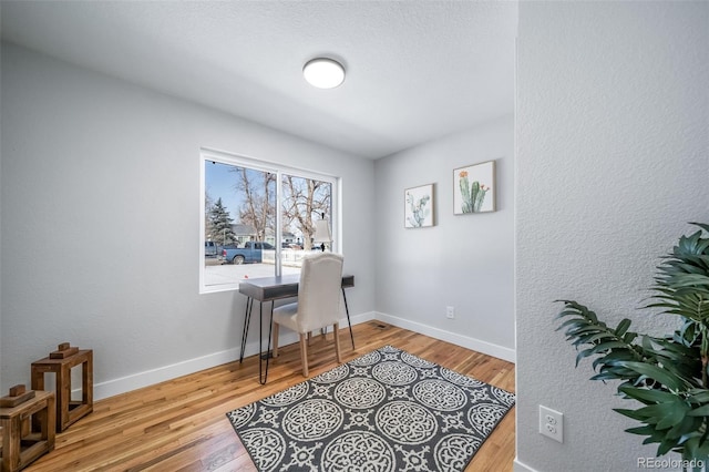 office area featuring baseboards, a textured wall, and light wood-style floors