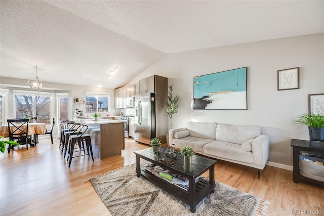 living room featuring a textured ceiling, light hardwood / wood-style flooring, a chandelier, and vaulted ceiling