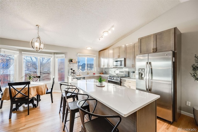 kitchen with stainless steel appliances, vaulted ceiling, decorative light fixtures, light hardwood / wood-style flooring, and a center island