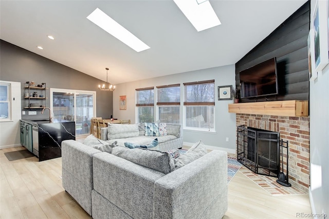 living area with vaulted ceiling, light wood finished floors, a chandelier, a brick fireplace, and a skylight
