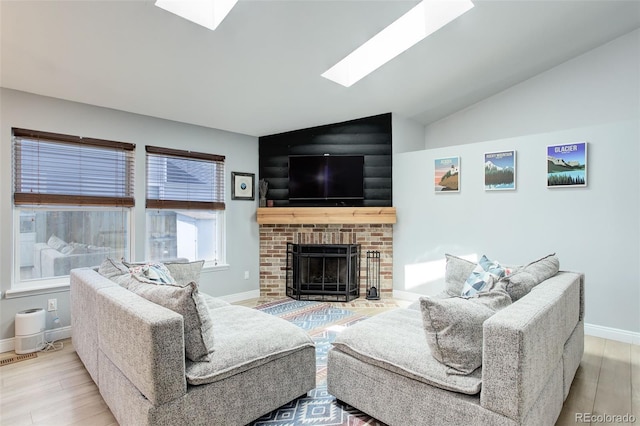 living area featuring a skylight, wood finished floors, baseboards, a brick fireplace, and vaulted ceiling