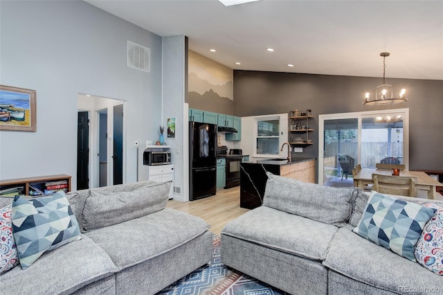 living room featuring a chandelier, high vaulted ceiling, light wood-type flooring, and recessed lighting