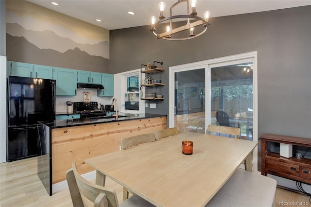 kitchen featuring black appliances, blue cabinetry, a chandelier, under cabinet range hood, and dark countertops