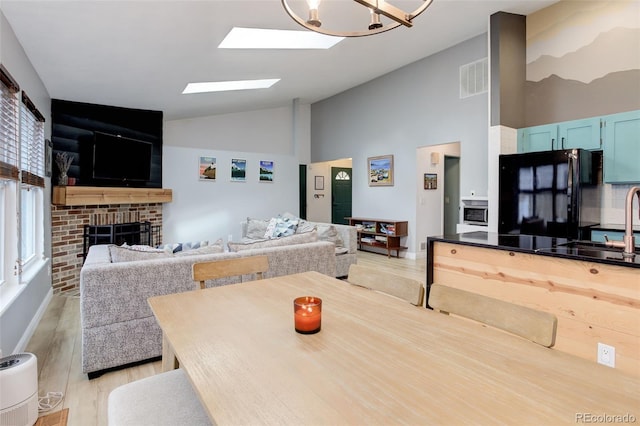 dining area with light wood-style flooring, high vaulted ceiling, a brick fireplace, a skylight, and baseboards
