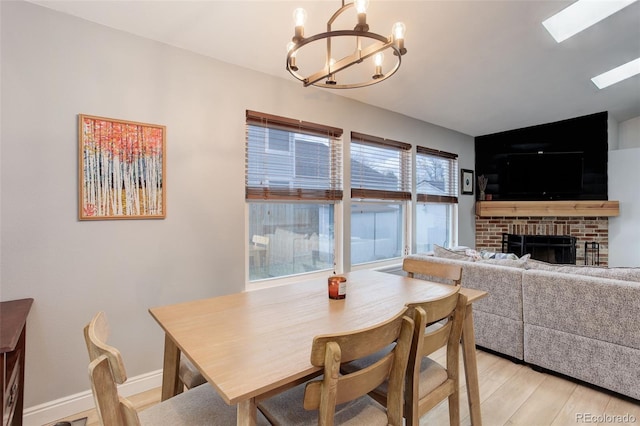 dining space with a chandelier, a brick fireplace, light wood-style flooring, and baseboards